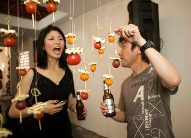 two people standing next to each other with food hanging from strings in front of them