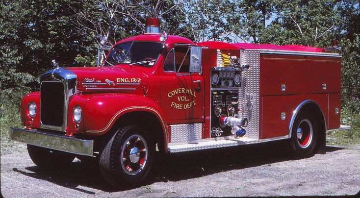 a red fire truck parked on top of a dirt road next to trees and bushes