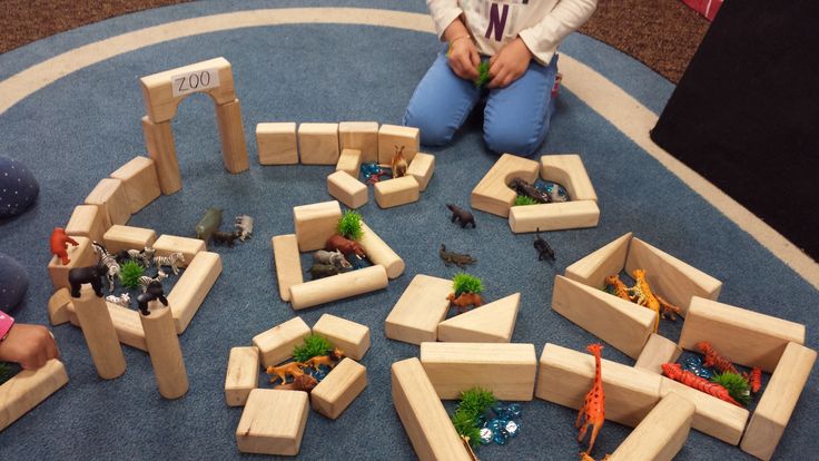 a child sitting on the floor playing with wooden blocks and toy animals in front of them