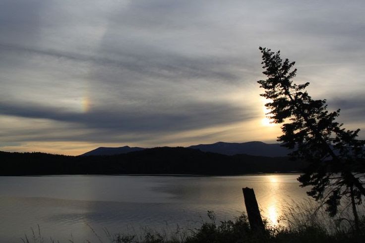 the sun is setting over a lake with mountains in the distance and trees to the side