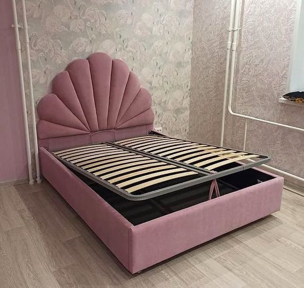 a pink bed frame with an open drawer underneath it in the middle of a room