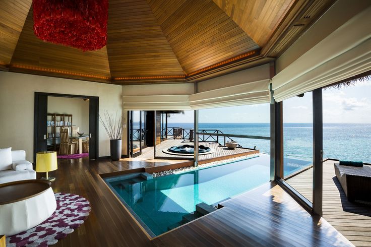 an indoor swimming pool in the middle of a wooden floored room with large windows overlooking the ocean