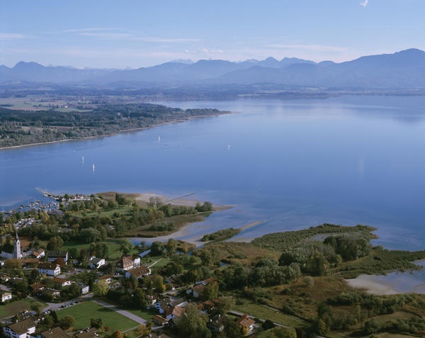 an aerial view of a lake with mountains in the distance and houses on the other side