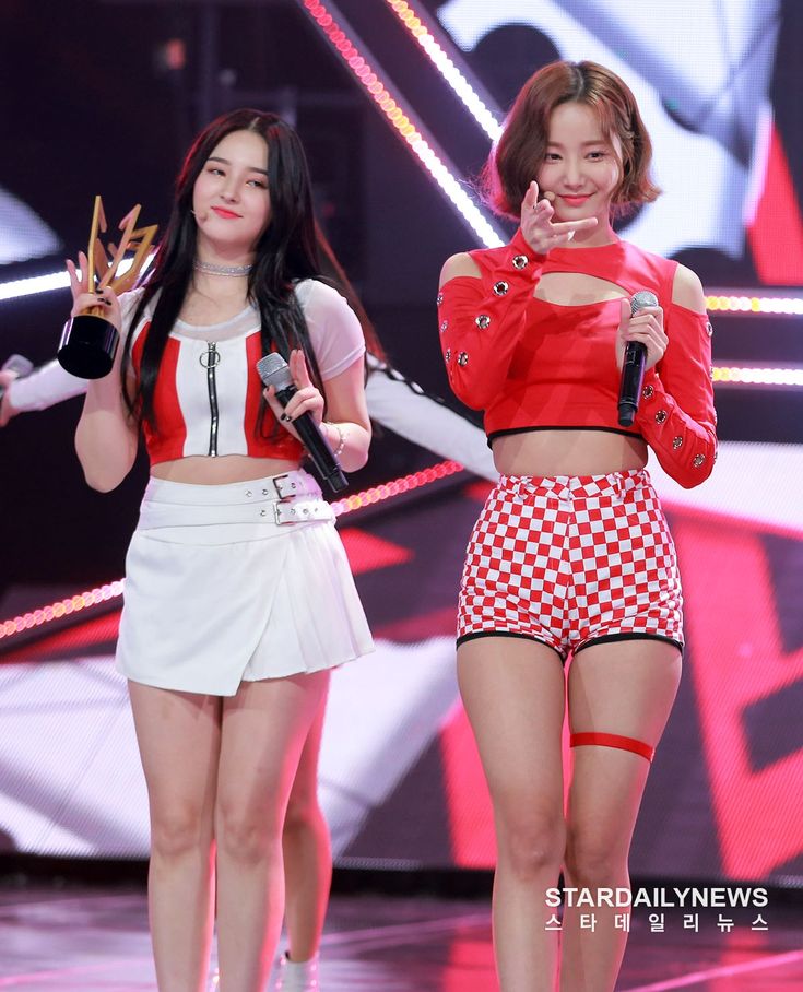 two girls in red and white outfits on stage with microphones, one holding up her hand