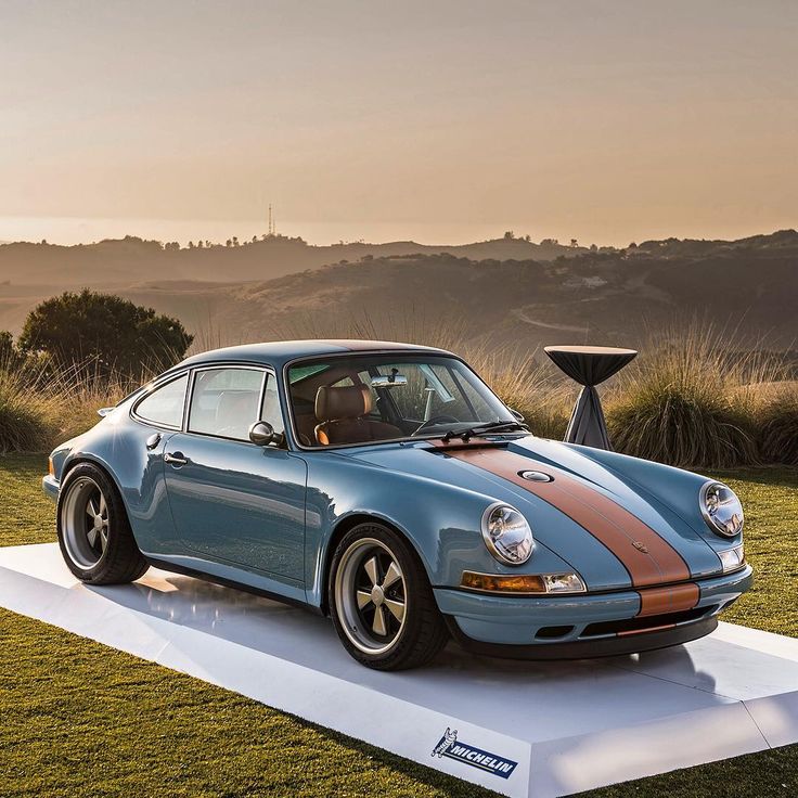 a blue car parked on top of a white platform in front of some grass and trees