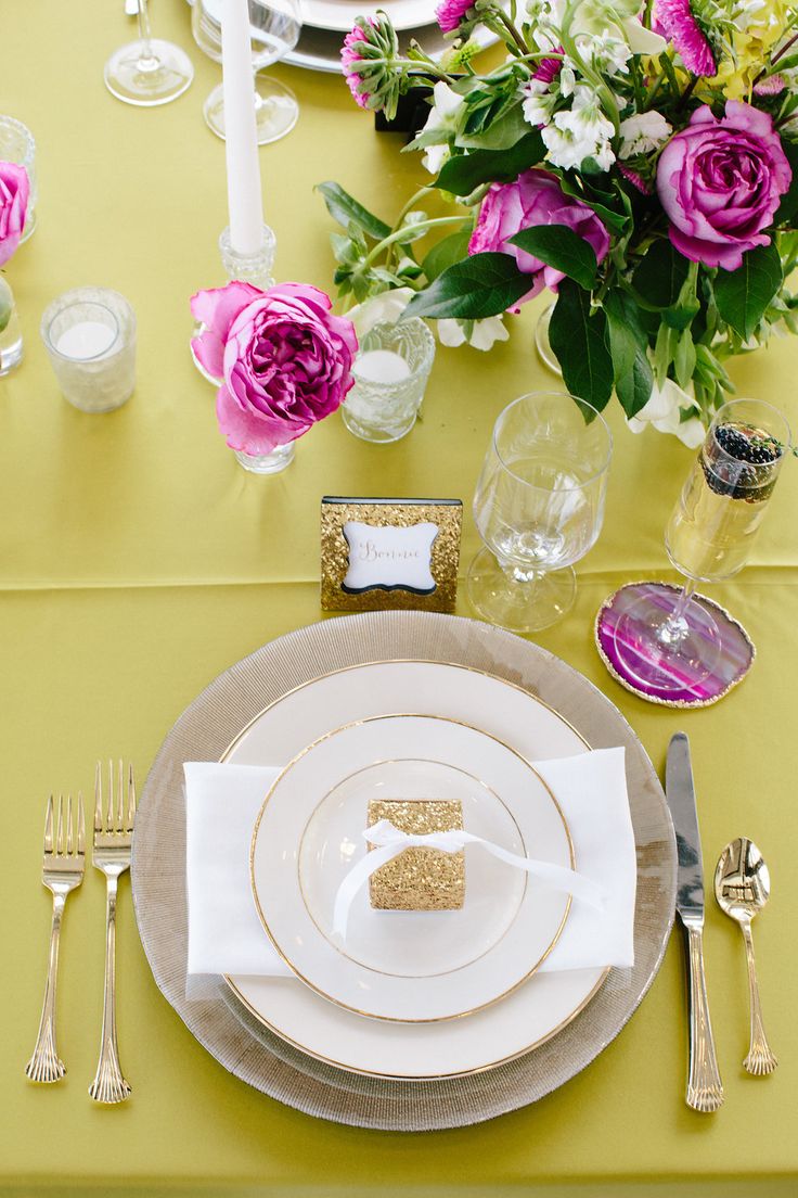 the table is set with gold and white plates, silverware, and pink flowers