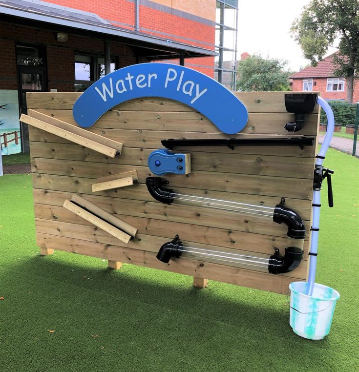 a water play area with wooden planks and pipes on the wall, in front of a brick building