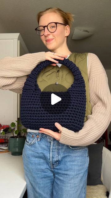 a woman is holding up a knitted bag