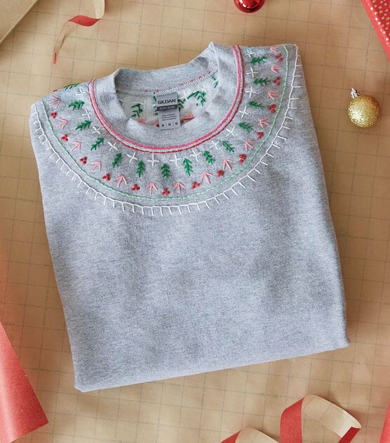 a gray sweater with christmas decorations and ribbon on the table next to it is an ornament