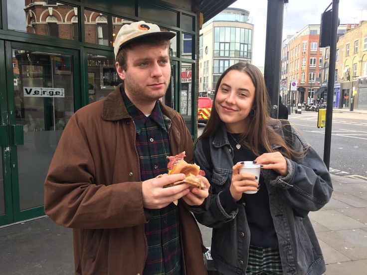 a man and woman standing next to each other holding hot dogs