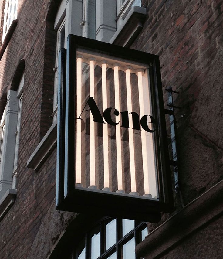 an acne sign hanging off the side of a building in front of a window