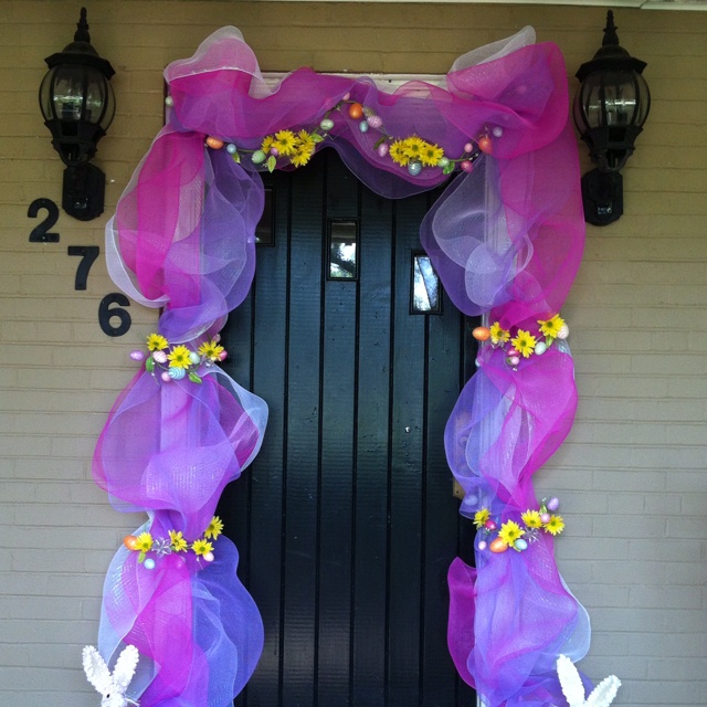 the front door is decorated with purple tulle and yellow flowers, while two white rabbits are standing in front of it