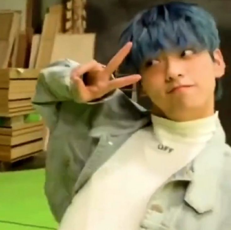 a man with blue hair making the peace sign