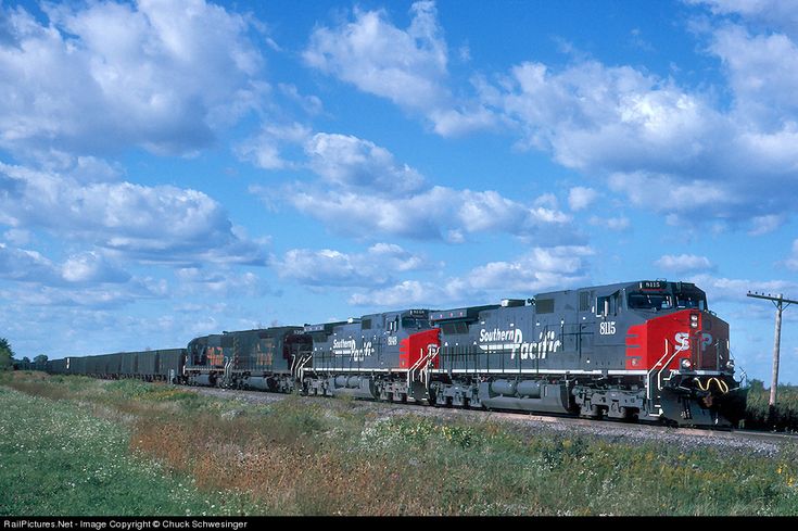 a train traveling down tracks next to a lush green field under a cloudy blue sky