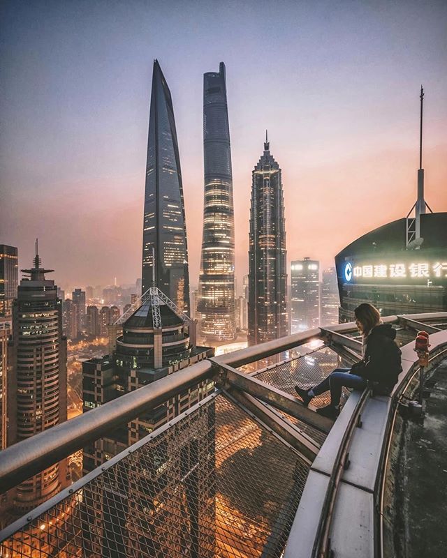 a man sitting on top of a metal railing next to tall buildings in the city