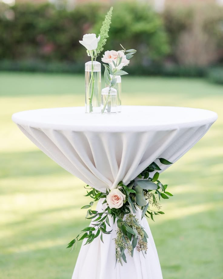 a white table with flowers and greenery on it in the middle of a field