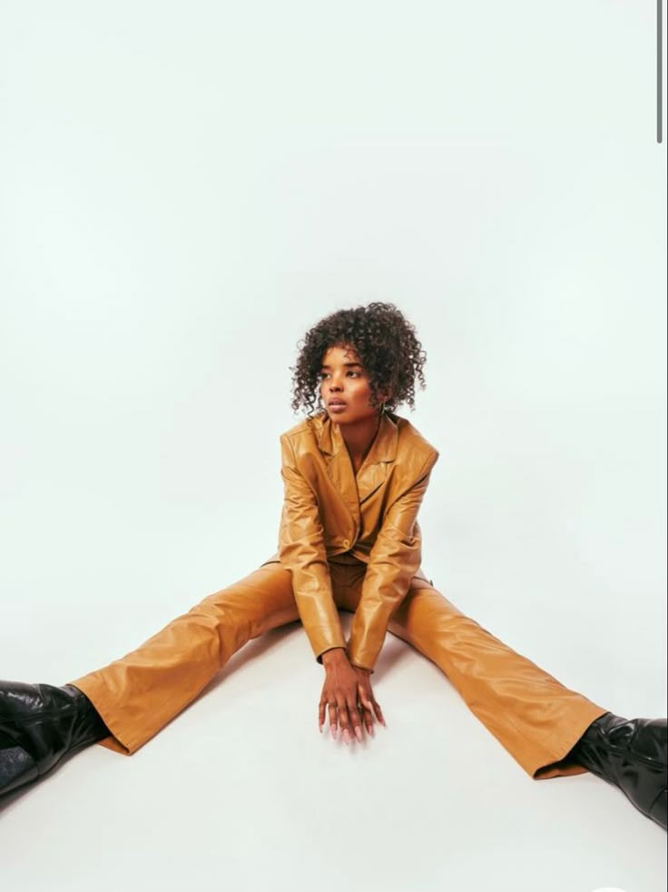 a woman sitting on the ground with her legs crossed, wearing brown leather pants and black boots