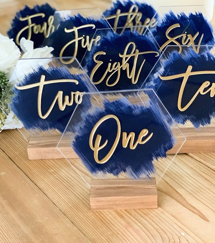 blue and gold acrylic place cards on wooden bases with flowers in the background