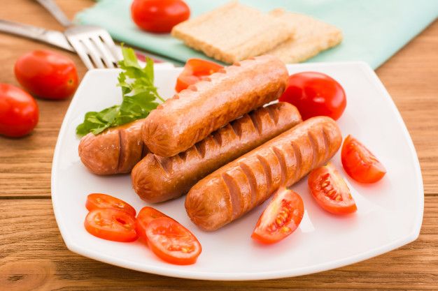 two sausages and tomatoes on a white plate with a fork next to some bread