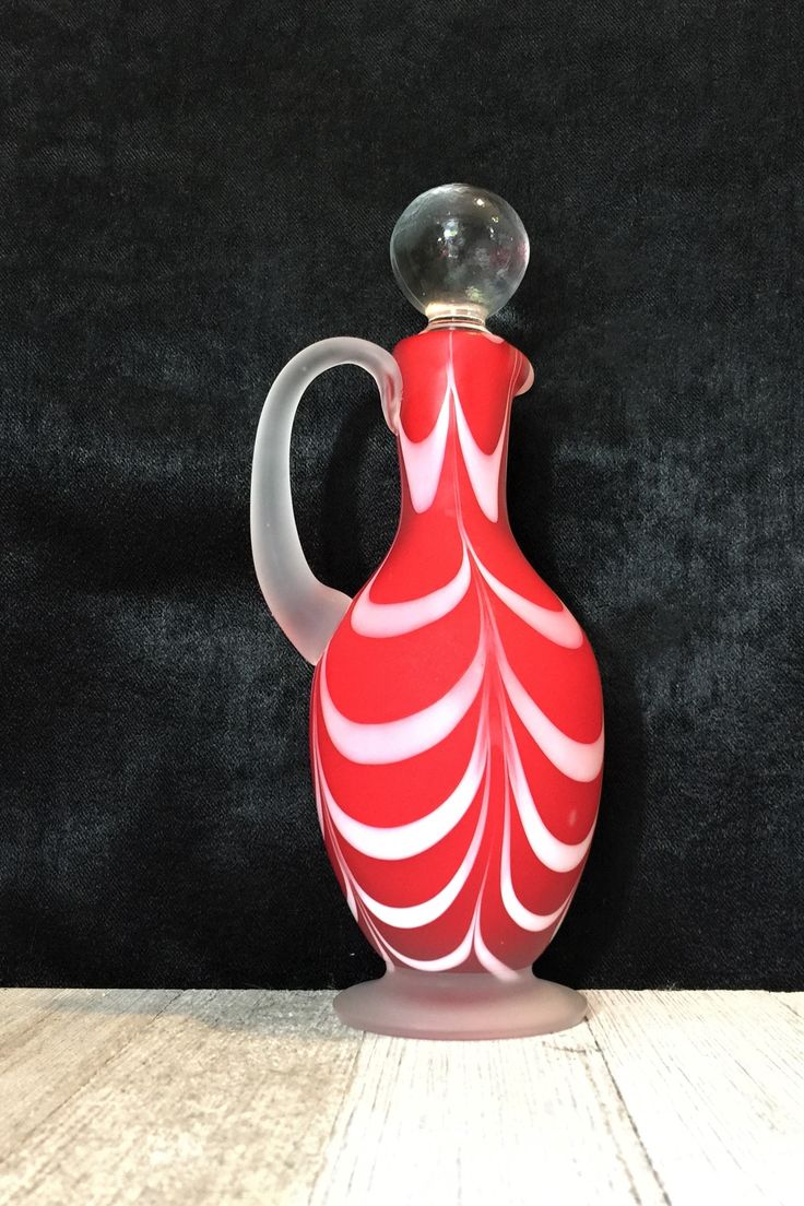 a red and white glass vase sitting on top of a wooden table next to a black wall