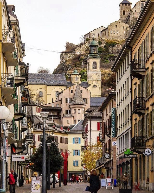 people are walking down the street in an old european city with buildings on both sides