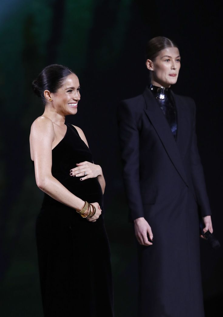 two people standing next to each other in front of a dark background and one person wearing a black dress