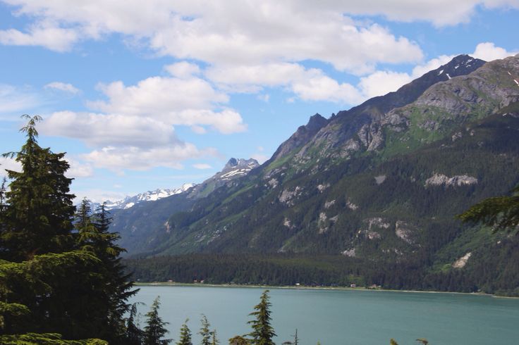 the mountains are covered in snow and green pine trees, with blue water below them