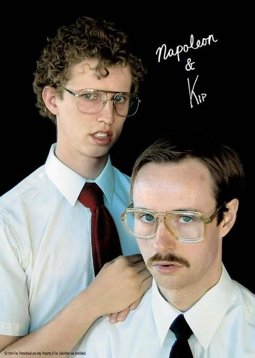 two young men with glasses and mustaches are posing for the camera, one is adjusting the tie on another man's neck