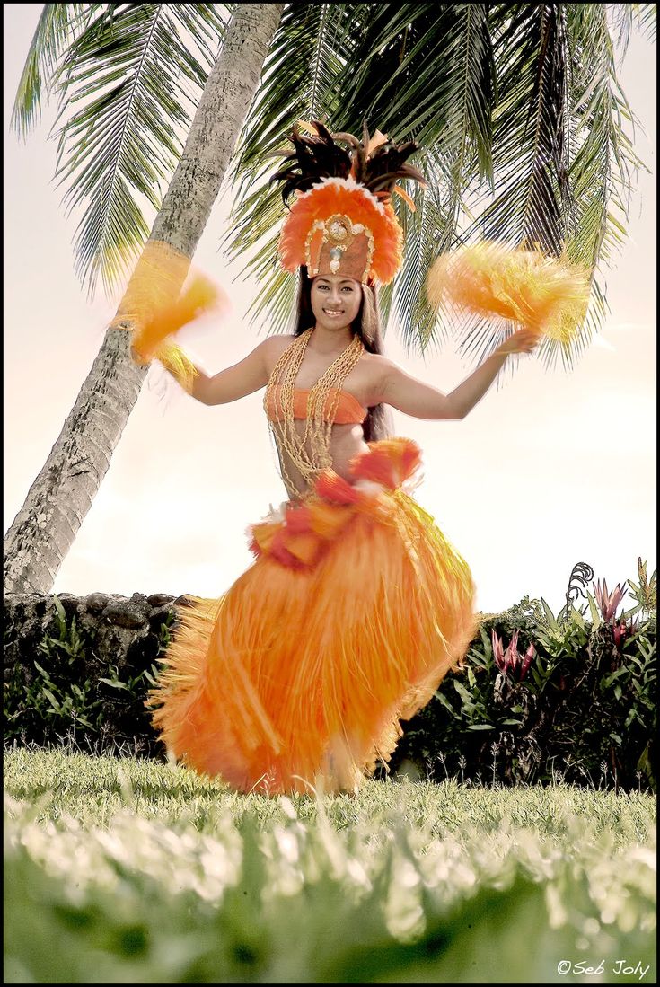 a woman in an orange dress and headdress is dancing under a palm tree