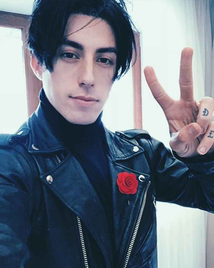 a man in a leather jacket making the peace sign with his hand and wearing a rose on it