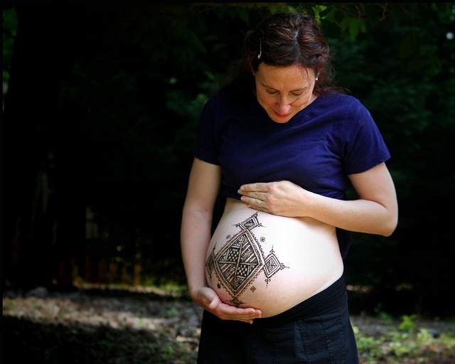 a pregnant woman is holding her belly with an intricate tattoo on it's stomach