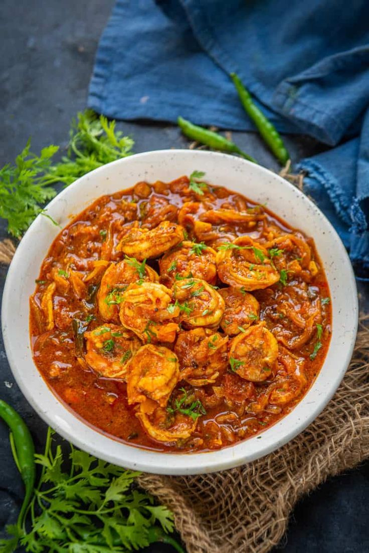 a white bowl filled with shrimp and tomato sauce on top of a blue table cloth