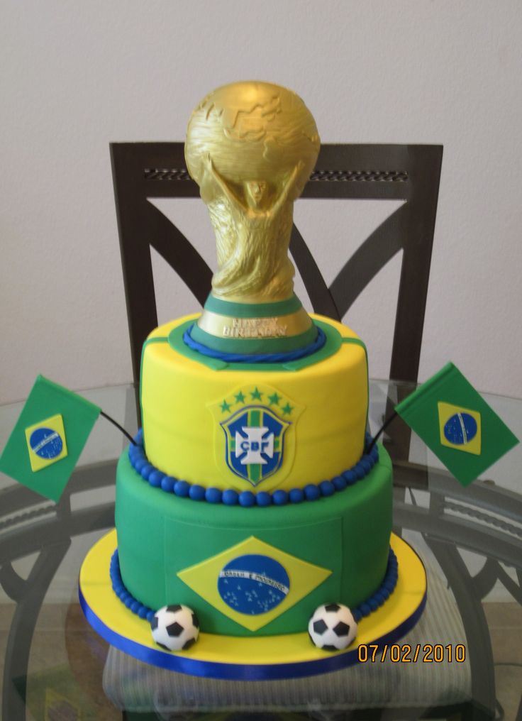 the cake is decorated with soccer balls and a golden trophy on it's head