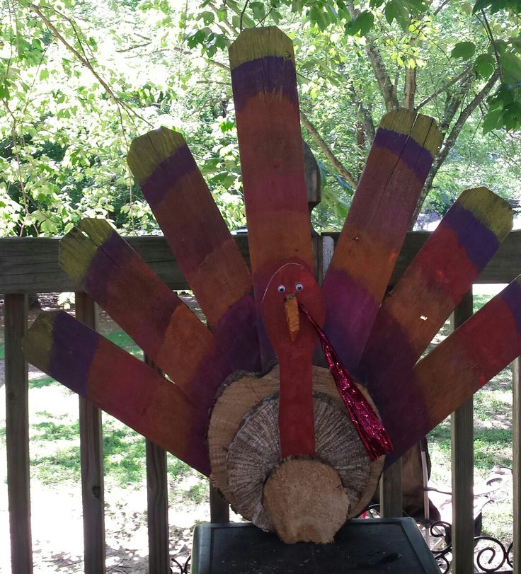 a wooden turkey sitting on top of a table next to a tree branch and fence