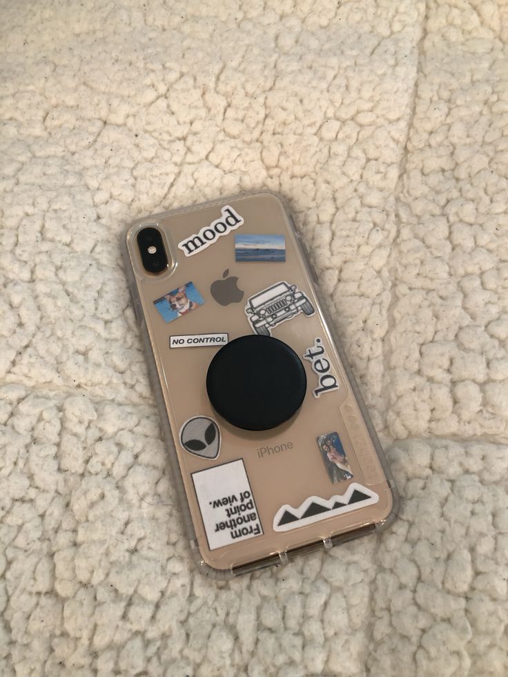 an iphone case with stickers on it sitting on a bed covered in white blankets