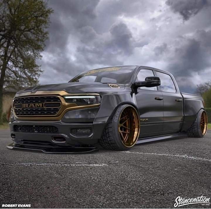 a black truck with gold rims parked in a parking lot next to some trees