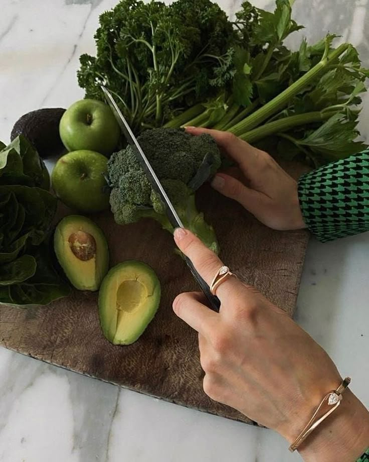 a person cutting up an avocado on top of a wooden board next to other fruits and vegetables