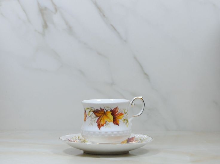 a cup and saucer with leaves painted on the side sitting on a marble surface