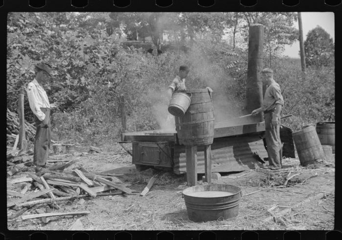 an old photo of two men pouring water from buckets in the woods, while another man looks on