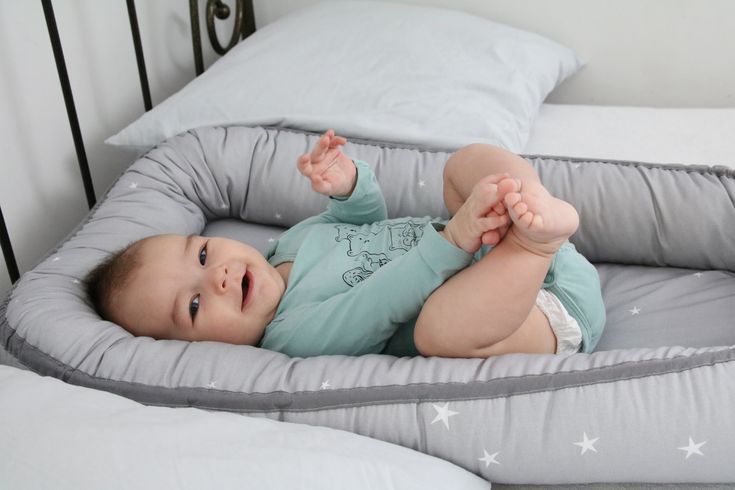 a baby laying in a bed with pillows on it's sides and his arms stretched out