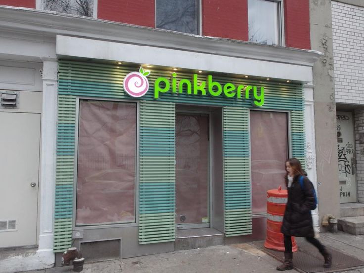 a woman walking past a store front with green and pink lettering on the side walk