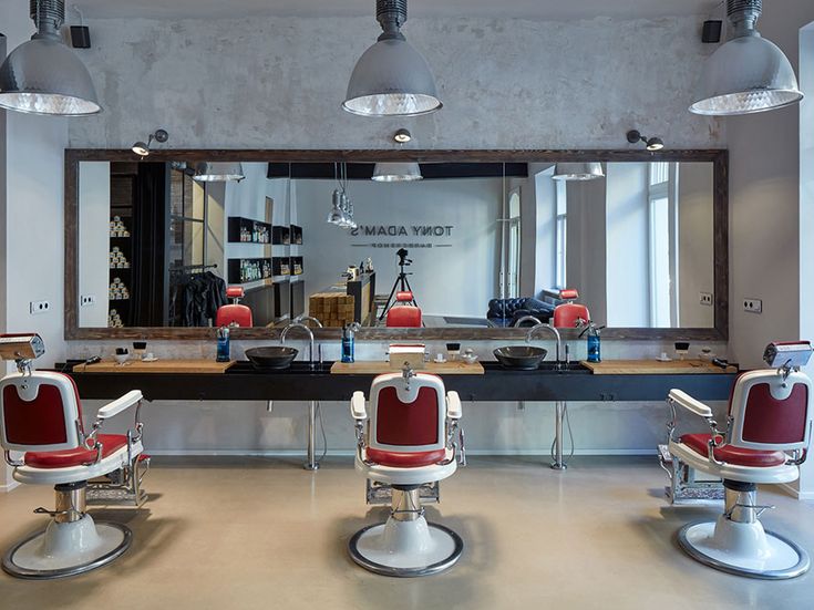 two red chairs sitting in front of a mirror with lights hanging from it's sides