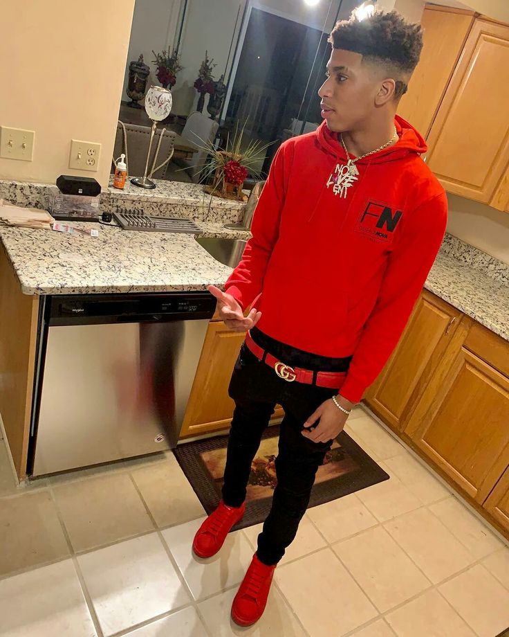 a young man in a red hoodie and black pants stands on the kitchen floor