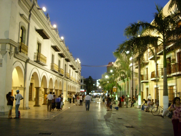 many people are walking down the street in front of some buildings at night with palm trees