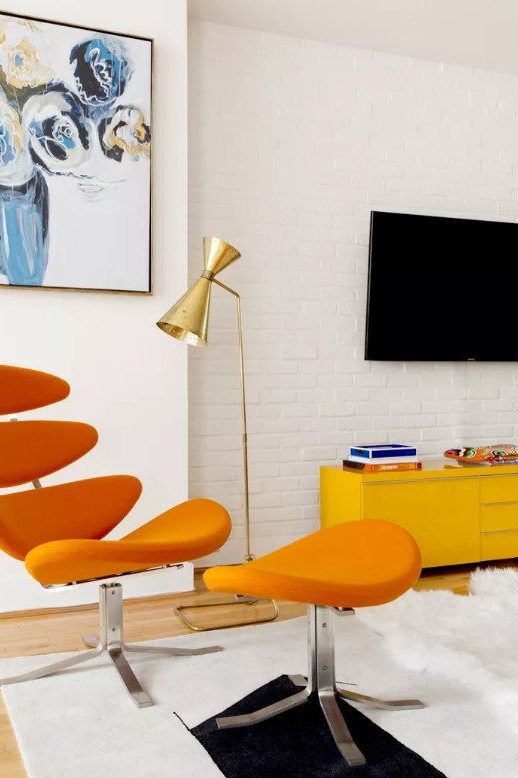 an orange chair and ottoman in front of a flat screen tv on a white brick wall