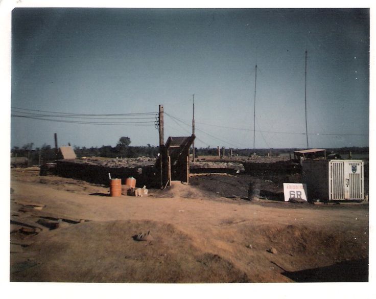 an old photo of a dirt road with buildings and telephone poles in the background on a sunny day