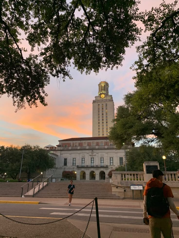 two people are walking up the steps in front of a building with a clock tower