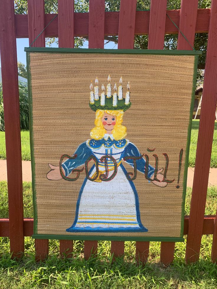 a wooden sign with a painting of a woman holding a lit candle on top of it