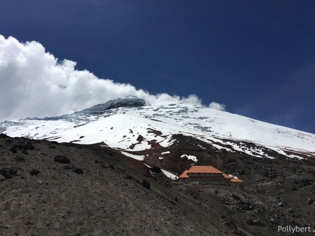 there is a snow covered mountain with a house in the foreground and clouds in the background