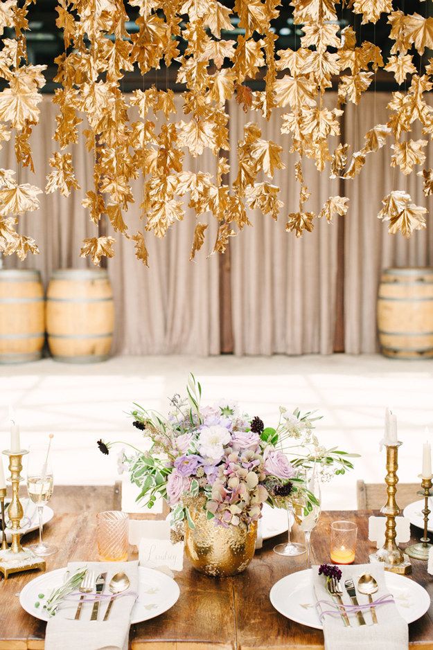 a wooden table topped with white plates covered in flowers and gold leaf chandelier